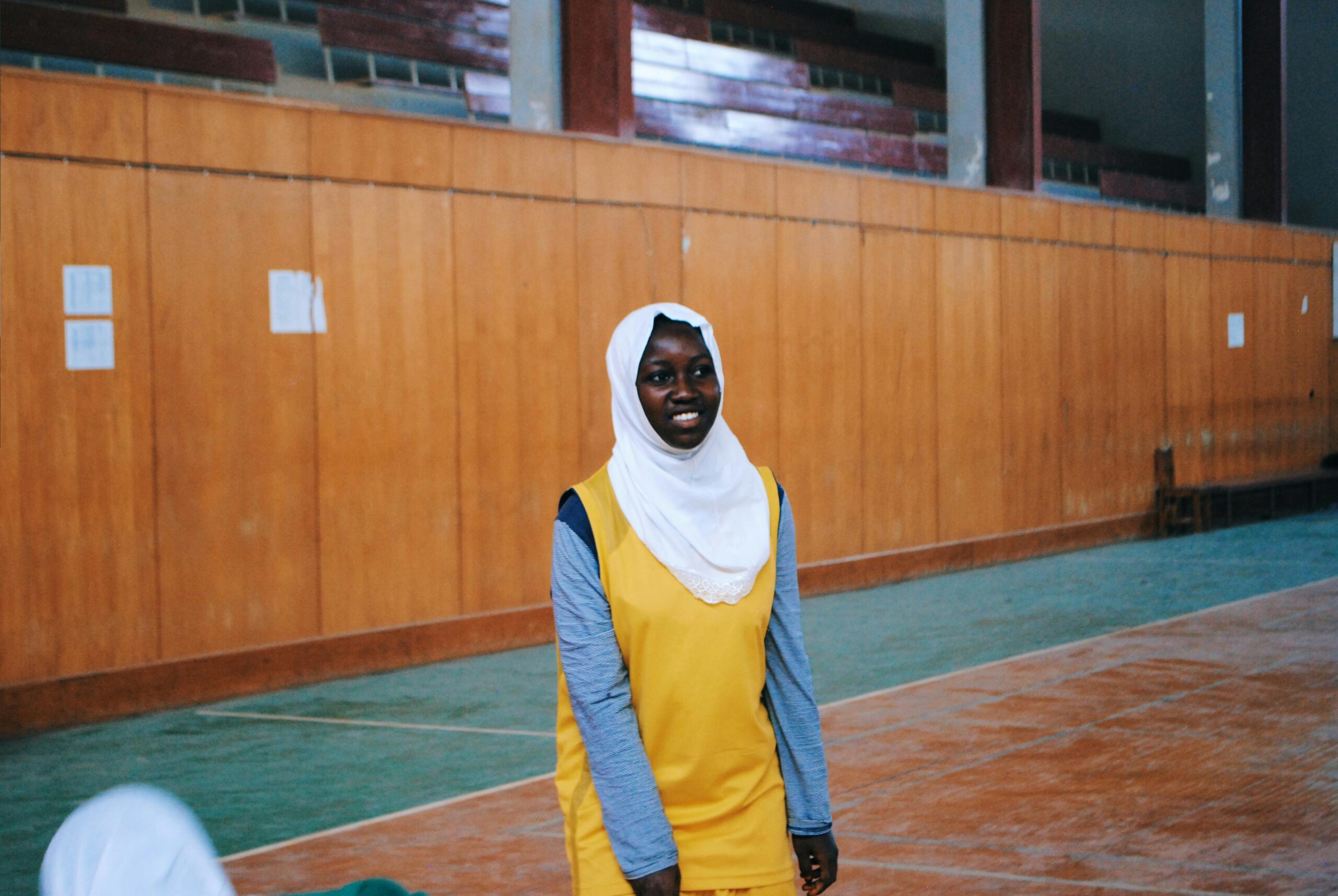 A young woman in a yellow outfit smiles indoors at a sports arena.